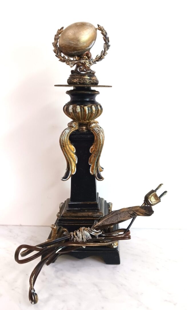 The Golden Egg is presente in a lofty position upon an ornate pedestal. The wrapped electric cord implies that energy travels to the lamp pedestal. However this is the Lamp of the Golden Goose. No such logic operates here. Just the beauty of the Golden Egg.